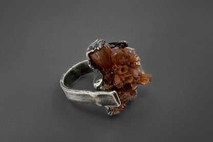 Silver ring with a brown aragonite crystal on a dark gray background